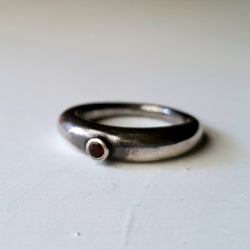 slim rounded band tapered to a narrow  base. ring is set with a single round pink rhodalite garnet in tube setting